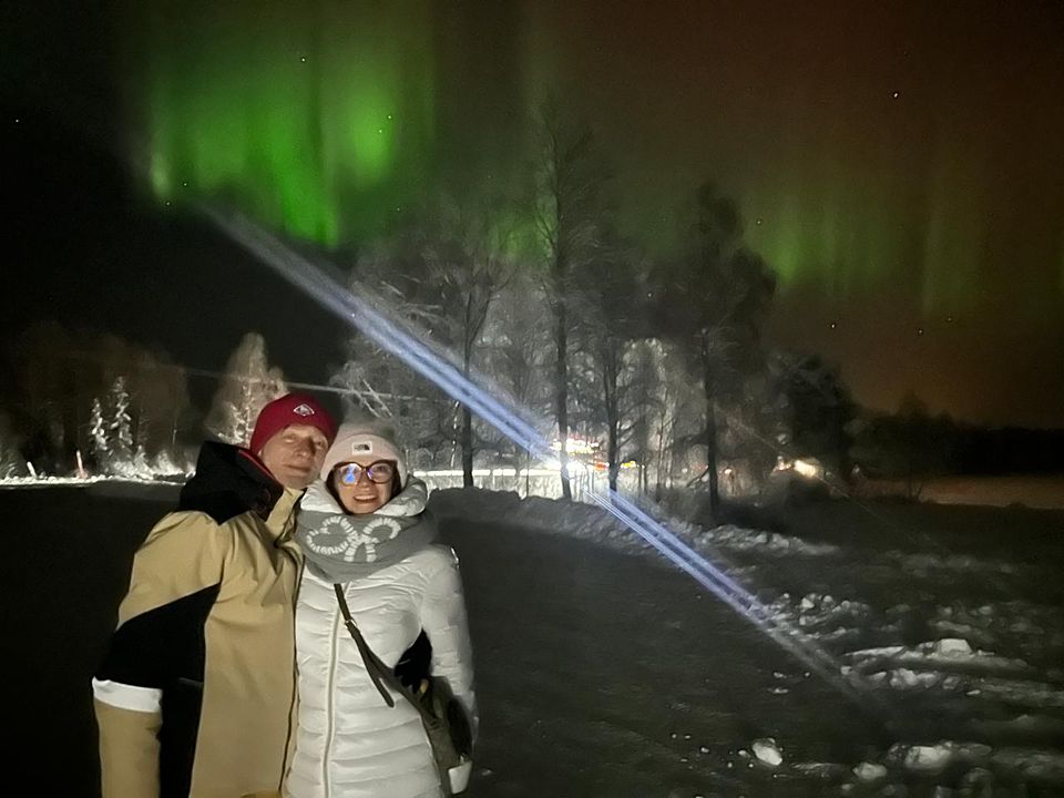 A couple in front of frosted trees with aurora and a beam of light behind