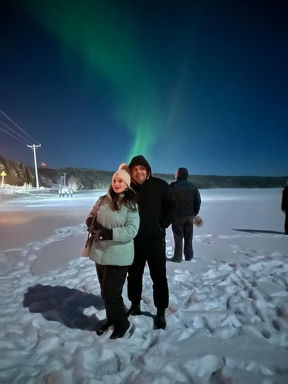 A couple on a moonlit frozen lake with a green aurora column behind them