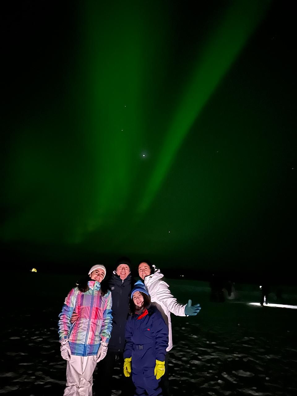 A group on a frozen lake beneath vertical aurora rays