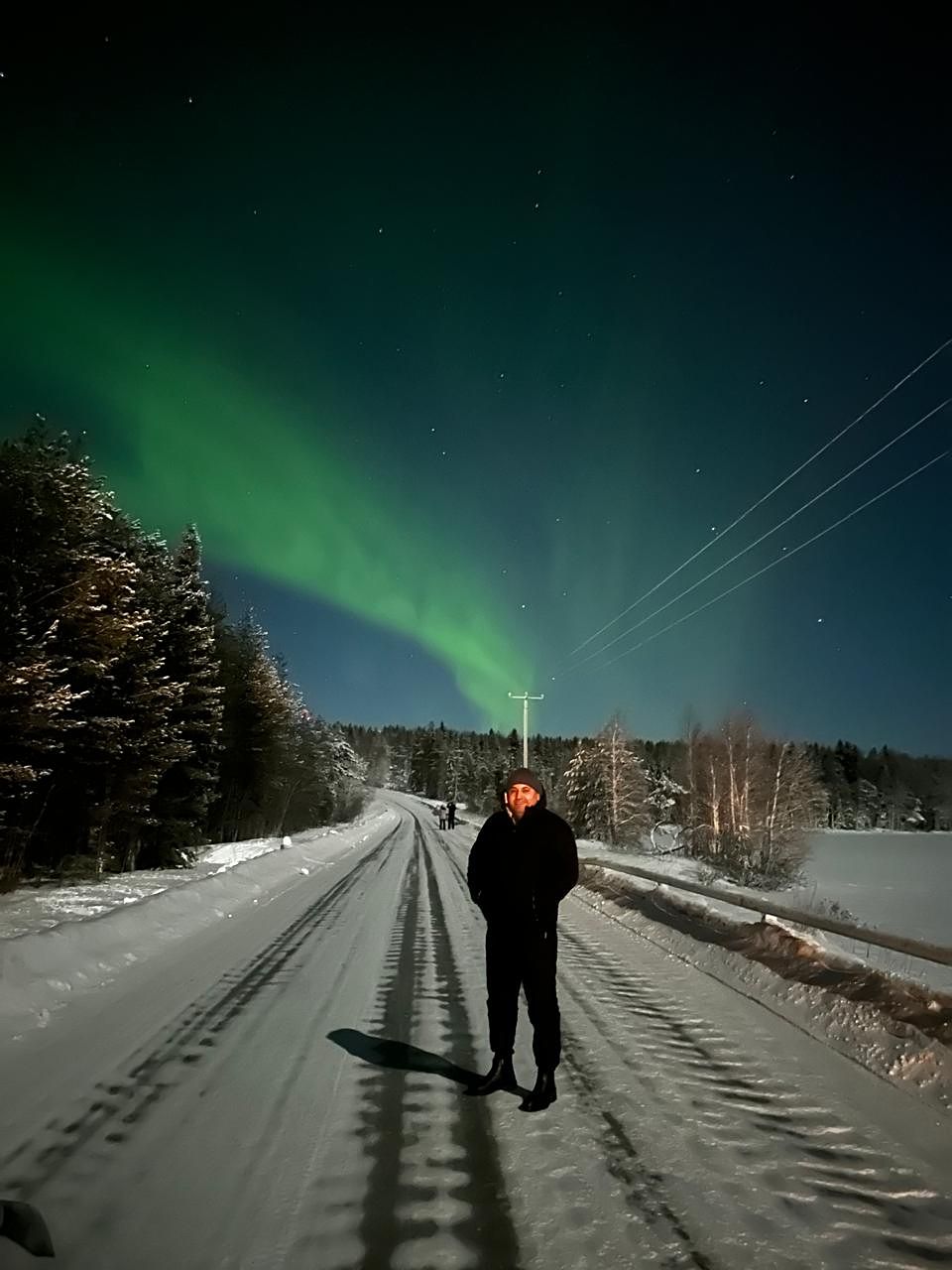 A guest standing in the middle of a snowy road beneath a wide aurora arc