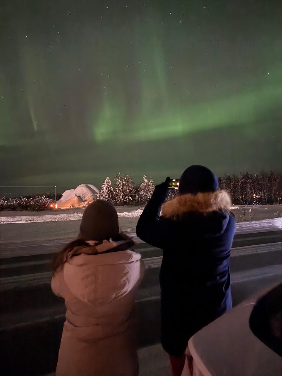 Two guests seen from behind, photographing the aurora from the roadside