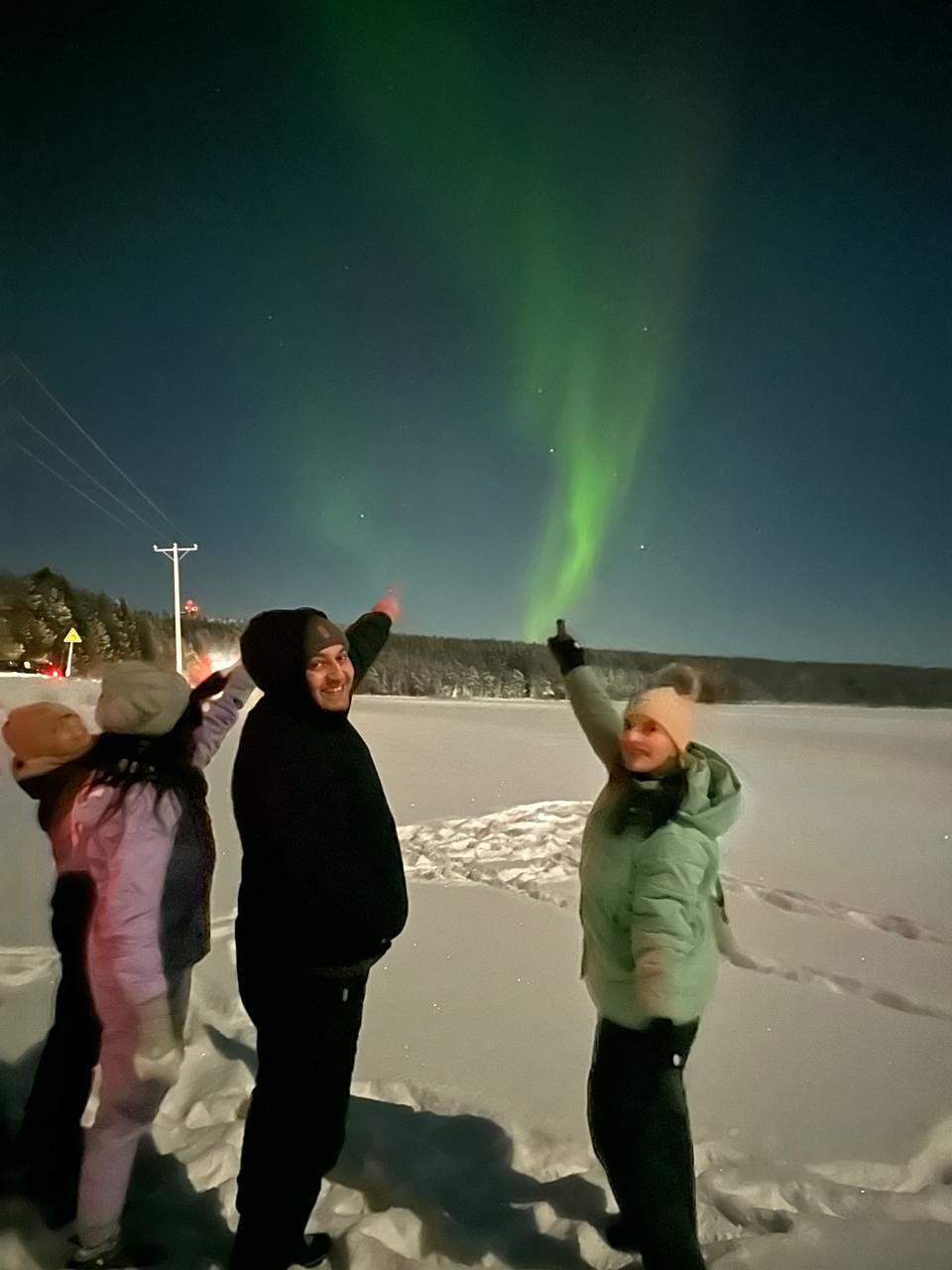 Guests pointing up at a green aurora column rising over a snow-covered lake