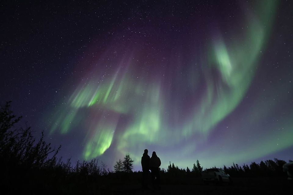 A couple in silhouette watching green and pink aurora curtains