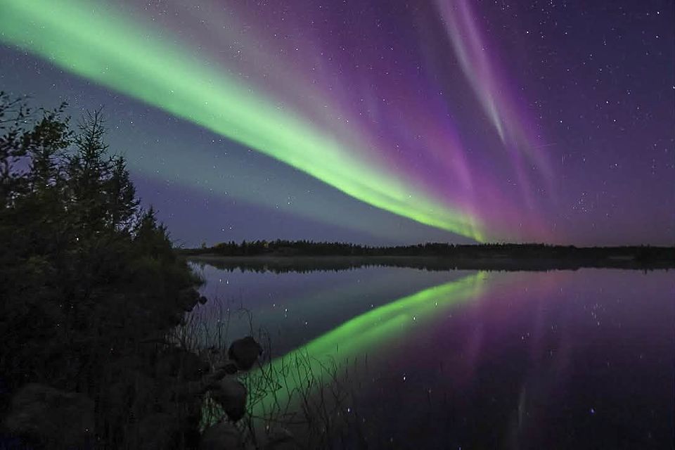 A green and violet aurora beam crossing the sky above a still lake