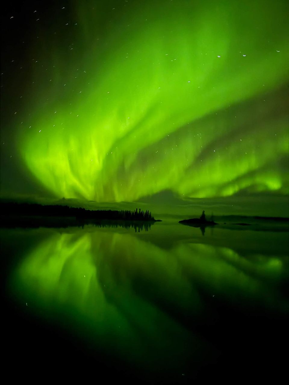 Lime-green aurora filling the sky over a small island, mirrored in the water